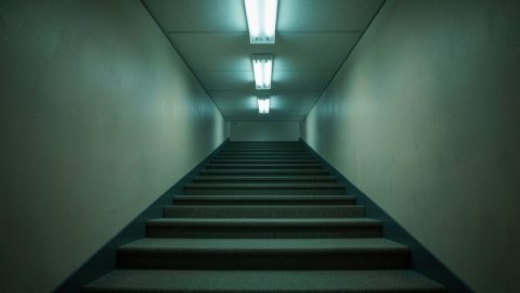 Conceptual illustration of a dim, endless carpeted stairwell of identical landings, evoking liminal-space unease