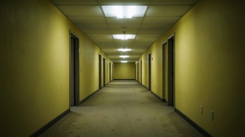 Conceptual illustration of an eerie empty yellow-walled office corridor with fluorescent lights, evoking liminal horror