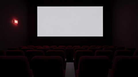 Conceptual illustration of a dim cinema auditorium with rows of empty seats and a faint exit-sign glow, evoking venue safety